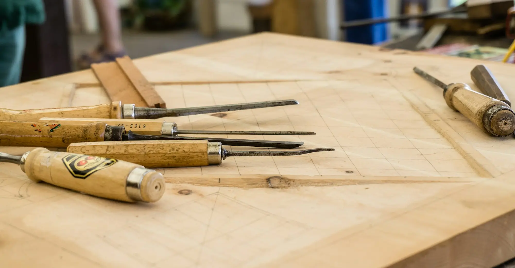 Wood chisels laid out on a timber workbench in a small furniture-making workshop, ready for work to restart