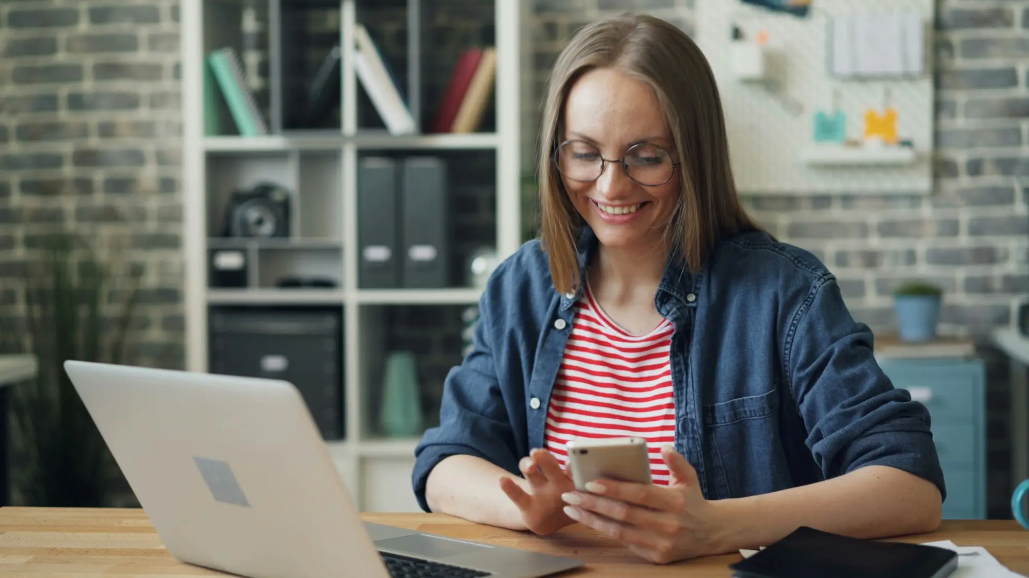 Business owner at her desk checking her identity app on a phone beside an open laptop